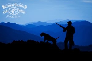 A person with a rifle stands beside a dog on a ridge, silhouetted against layered blue mountains at dusk. Waterfowl Unlimited Guide Service logo is in the top left corner.
