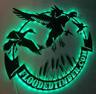 A metal sign with silhouettes of flying ducks, cattails, and the text "FLOODEDTIMBER.COM," illuminated by green LED lights.