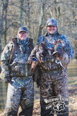 Two people in camouflage hunting gear stand outdoors, one holding several ducks. The logo "Waterfowl Unlimited Guide Service" is visible in the lower right corner.