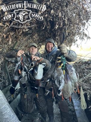 Two hunters in camouflage hold several harvested ducks inside a camouflaged blind. "Waterfowl Unlimited Guide Service" logo is displayed at the top of the image.